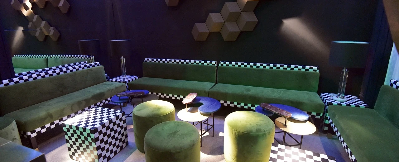 Moderne Loungegruppe mit grünen Samtsofas, schwarz-weißen Schachbrettmustern und geometrischen Wandpaneelen. Design von Christian JOBST.