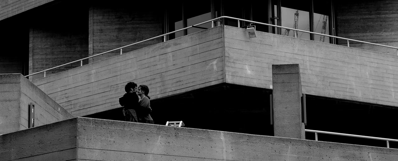 Schwarzweißfoto: Paar umarmt sich auf einer modernen Betonterrasse.