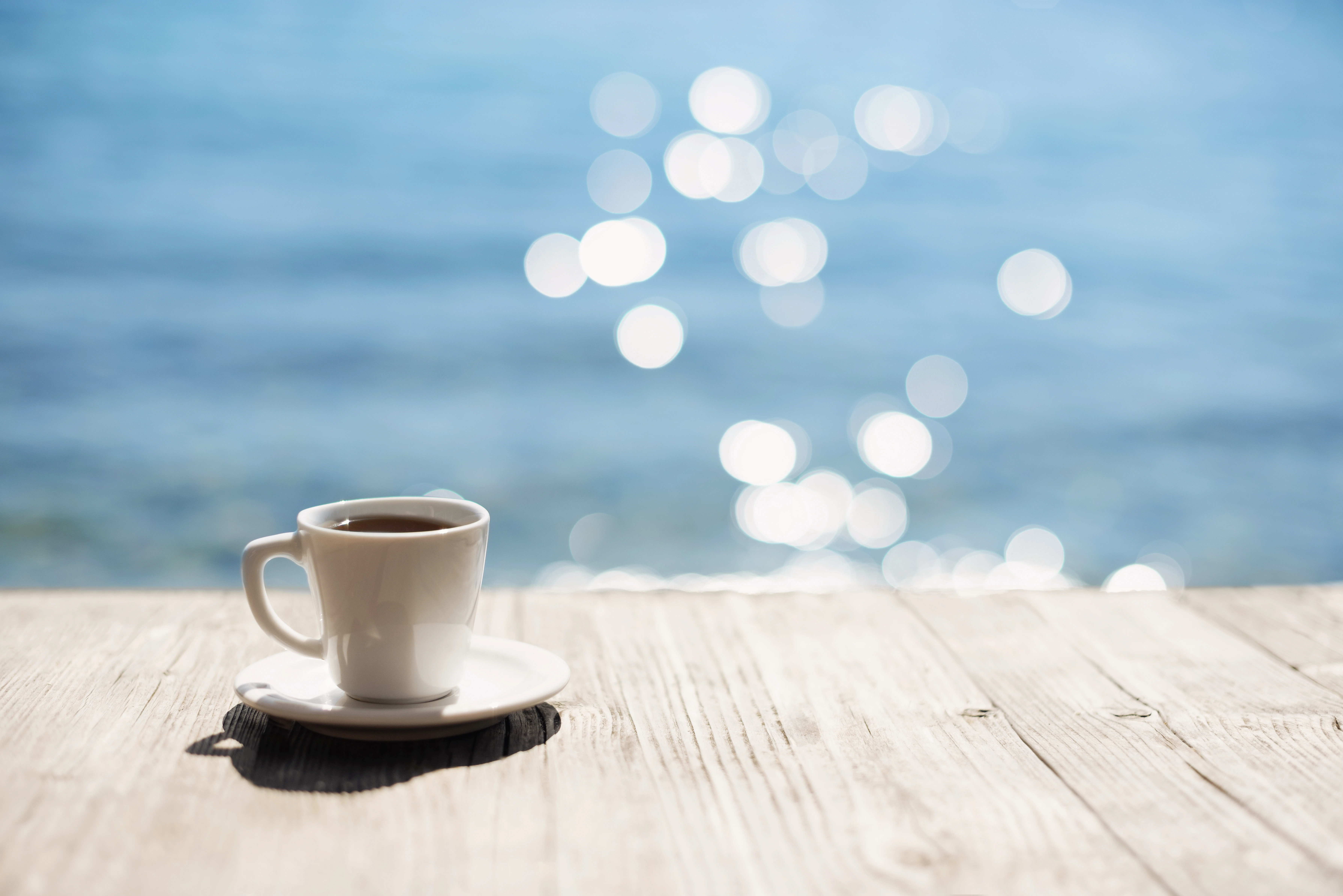 Espressotasse auf Holztisch vor sonnenbeschienenem See