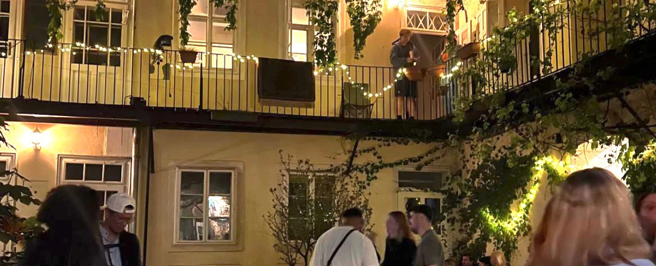 © Helena Erol Beleuchteter Innenhof bei Nacht mit Menschen und einem Balkon, geschmückt mit Lichterketten.
