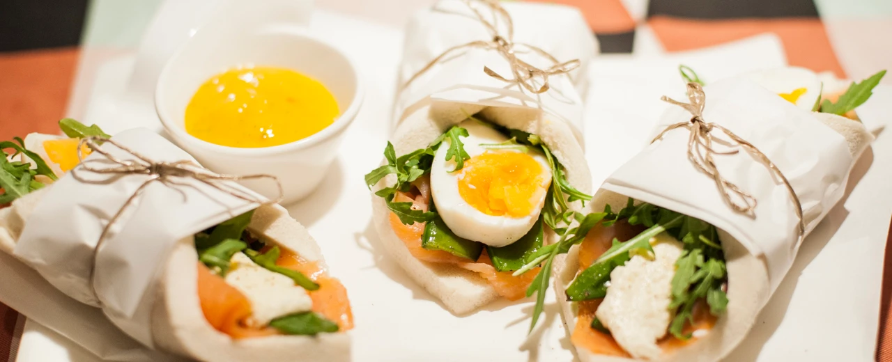 Drei Lachs-Wraps mit Ei, Rucola & Frischkäse, angerichtet mit einer orangenen Sauce.