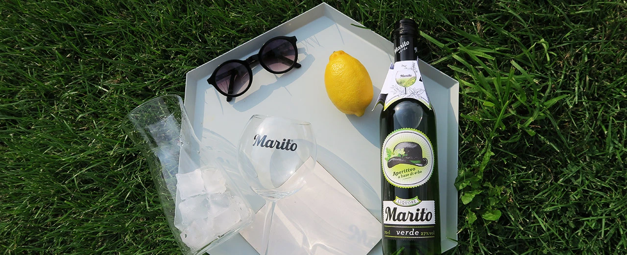 Flasche Marito Verde Likör auf Tablett mit Gläsern, Eis und Zitrone im Grünen.