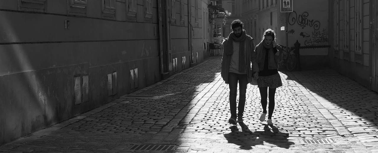 ©  Schwarz-weiß Foto: Paar geht Hand in Hand durch eine gepflasterte Gasse.  Sonnenlicht wirft Schatten.