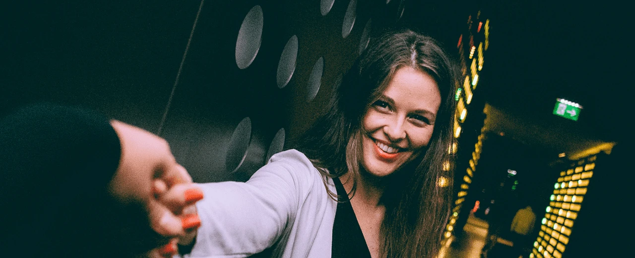 Lächelnde Frau mit langen braunen Haaren, die die Hand ausstreckt. Dynamisches Foto mit unscharfem Hintergrund.