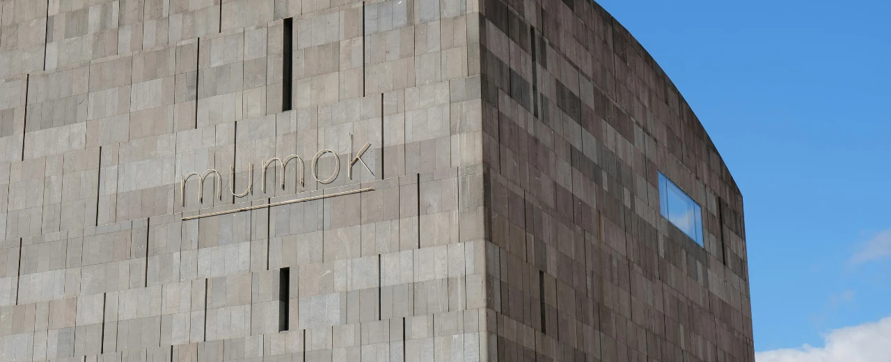 Ausschnitt der MUMOK-Fassade in Wien. Graue Steinplatten, goldene Schriftzug.