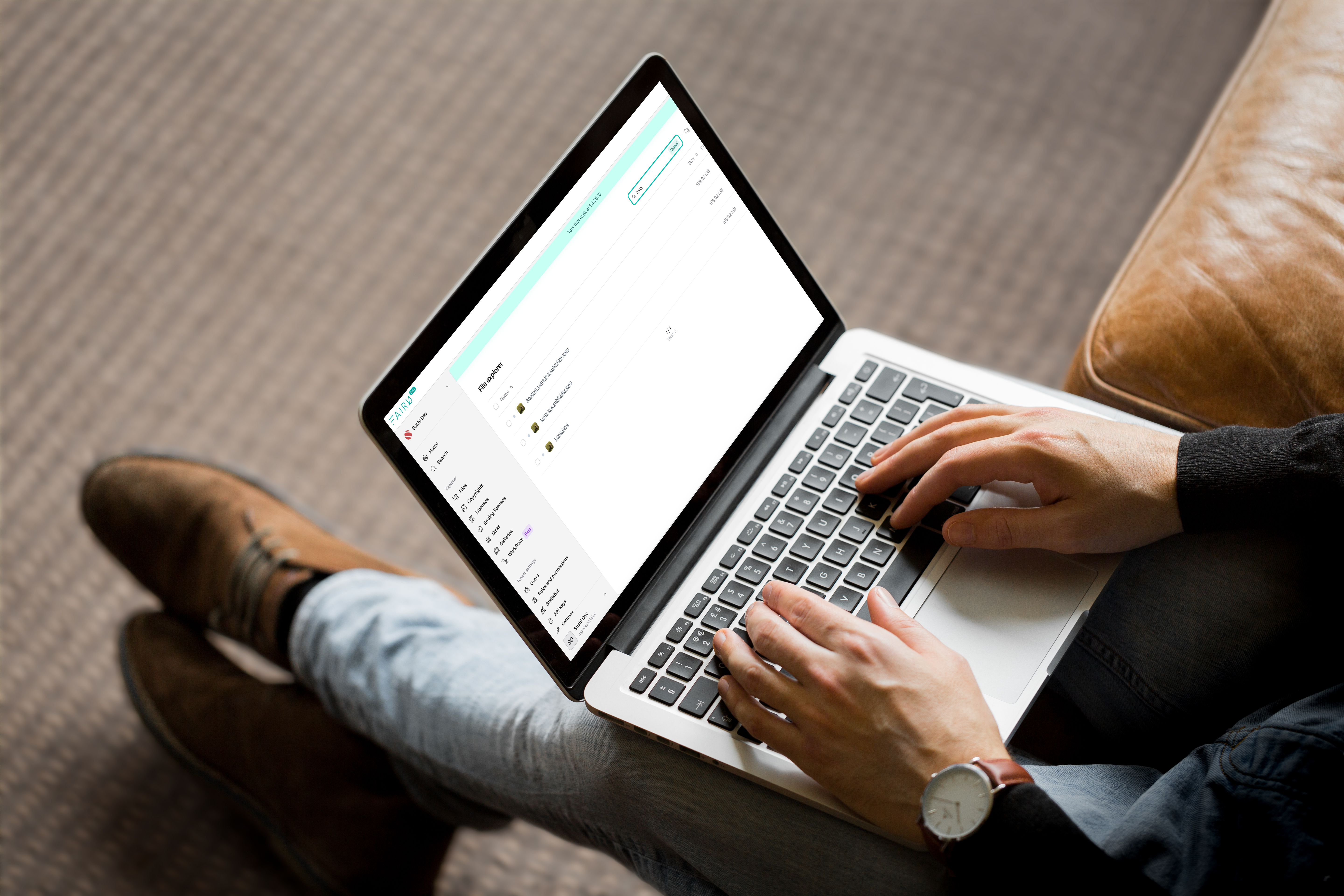 A person using a laptop computer displaying a digital asset management system interface while sitting down.