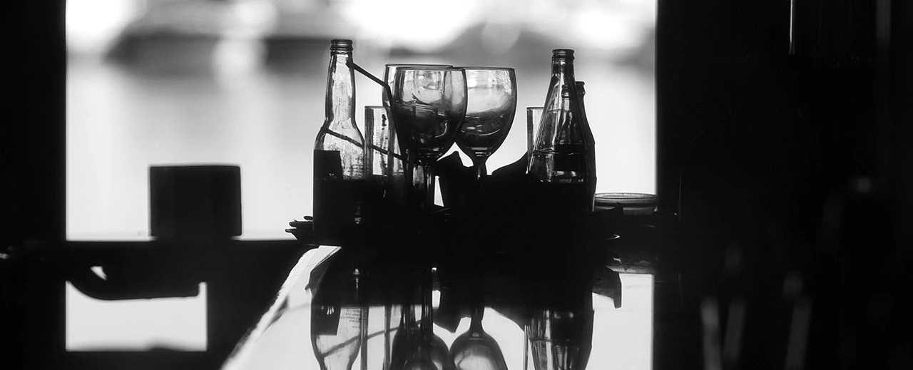 Schwarz-weiß Foto: Leere Gläser & Flaschen auf glänzender Oberfläche. Mit Adobe Lightroom bearbeitet.