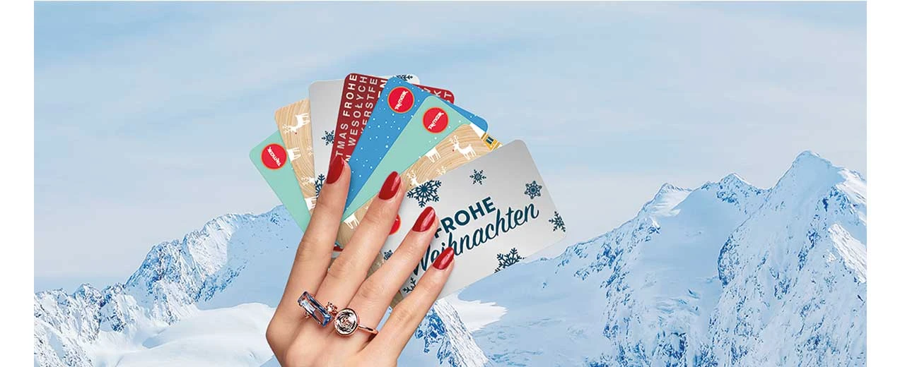 Hand mit mehreren Weihnachtsgeschenkkarten vor verschneiten Bergen. Frohe Weihnachten!