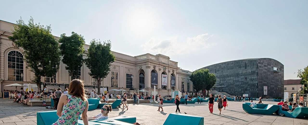 MuseumsQuartier Wien: Leopold Museum & MUMOK, sonniger Tag, Menschen entspannen auf modernen Sitzgelegenheiten.