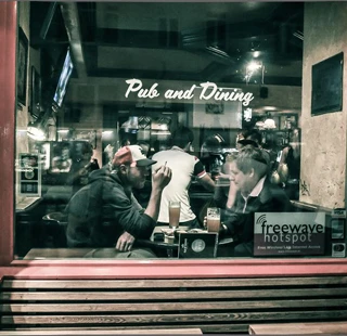 © Charlie P's Blick durch ein Fenster auf ein belebtes Pub mit Gästen an Tischen und dem Schriftzug