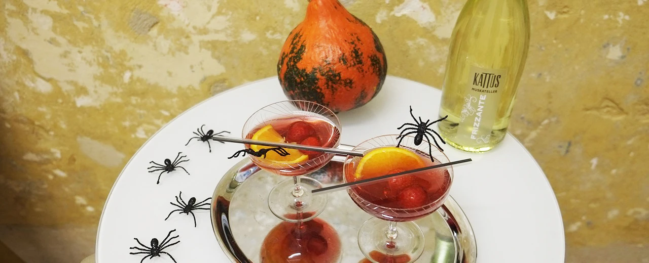 © Miriam Kummer Zwei rote Halloween-Cocktails mit Erdbeeren & Orangenscheiben, dekoriert mit Spinnen.  Kürbis & Frizzante-Flasche.