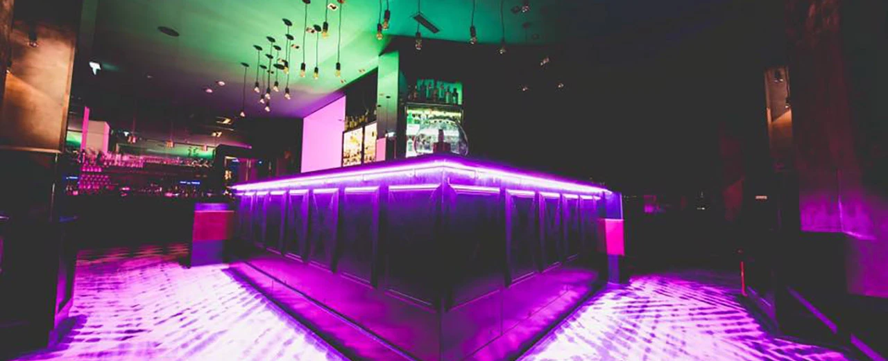 Moderne Bar mit purpurfarbener LED-Beleuchtung, dunklem Holz und Leder. Stilvolle Einrichtung für Nachtclub oder Lounge.